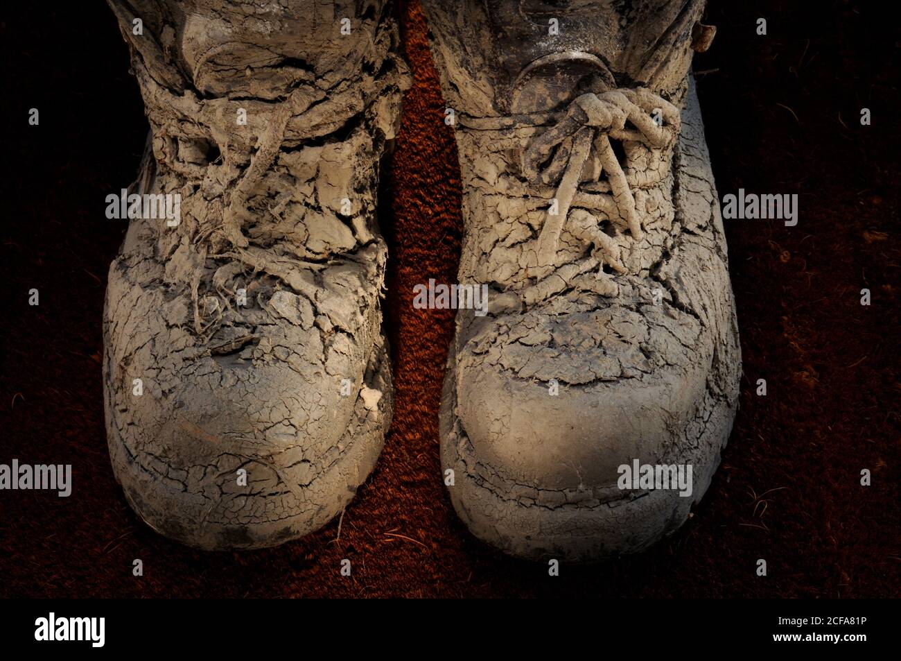 Pair of old worn walking boots covered in dried on thick mud with