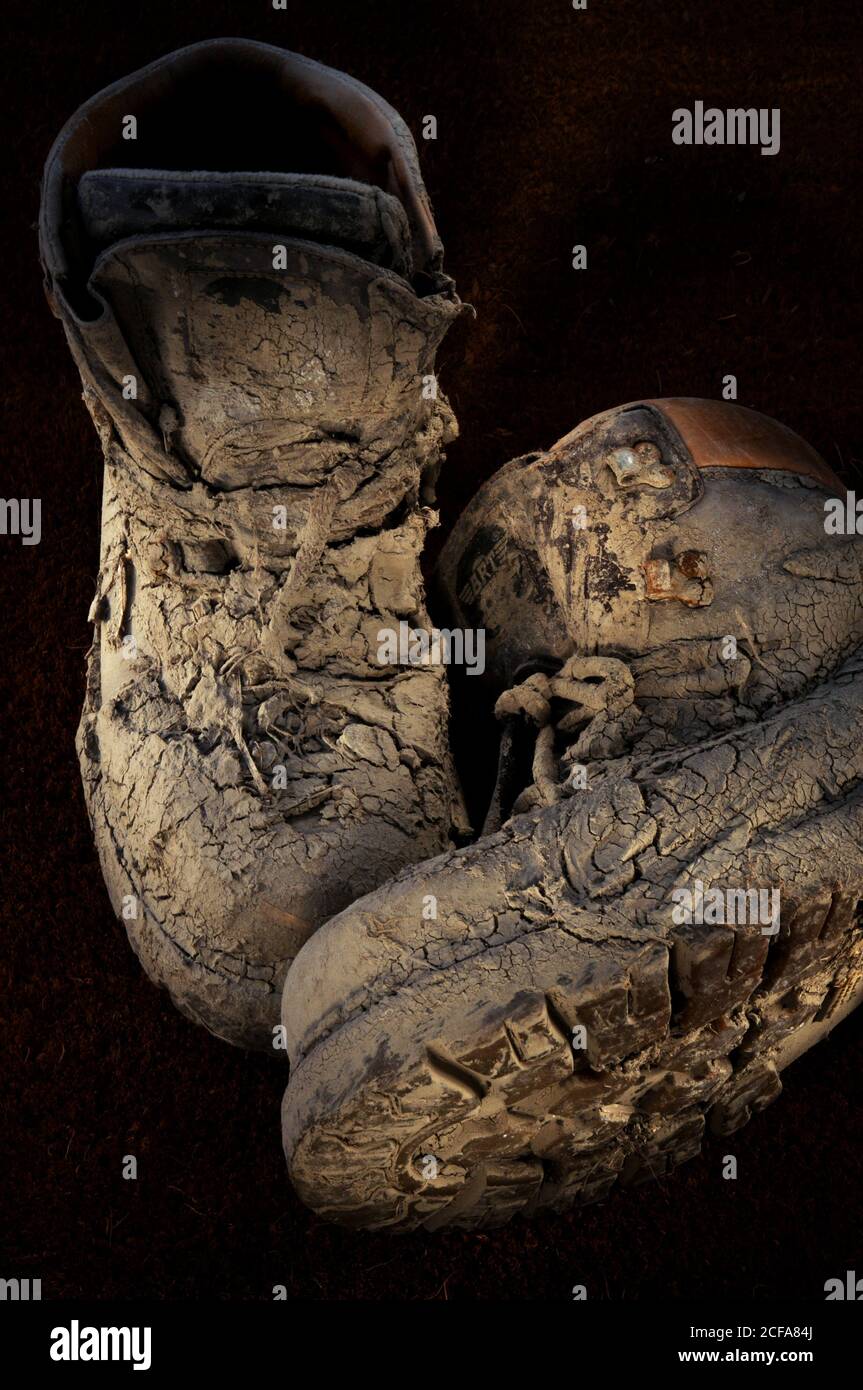 Pair of old worn walking boots covered in dried on thick mud with