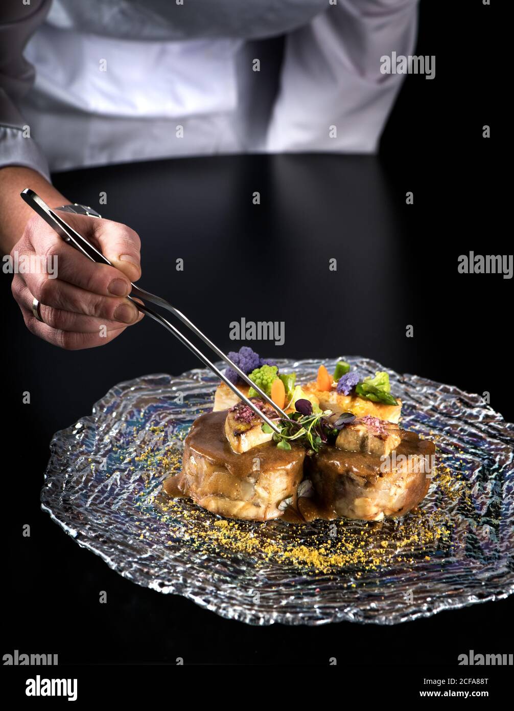 Crop anonymous chef with tongs garnishing gourmet organic sirloin steak ...