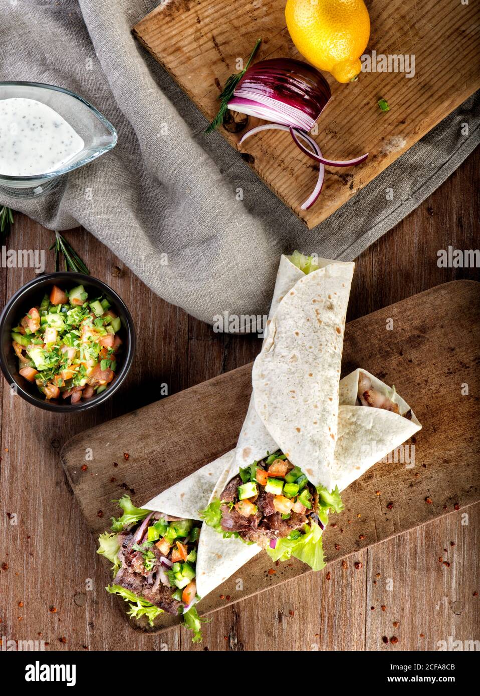 Top view of traditional Turkish snack durum made with wrapped flatbread filled with doner kebab with lamb meat and vegetables served on wooden table Stock Photo
