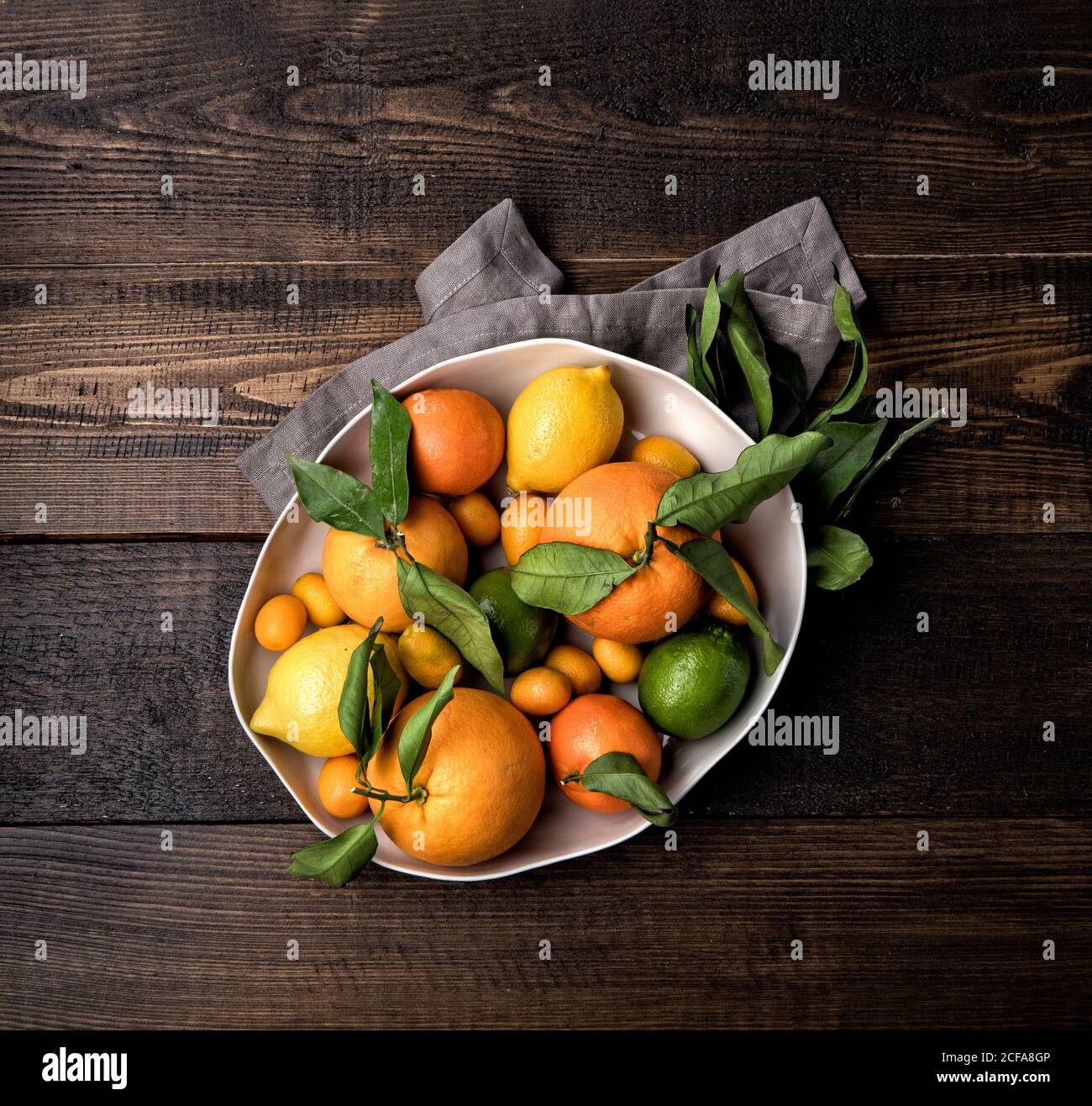 Top view of ripe oranges and mandarins placed in bowl with kumquat and lemon on wooden table with napkin Stock Photo
