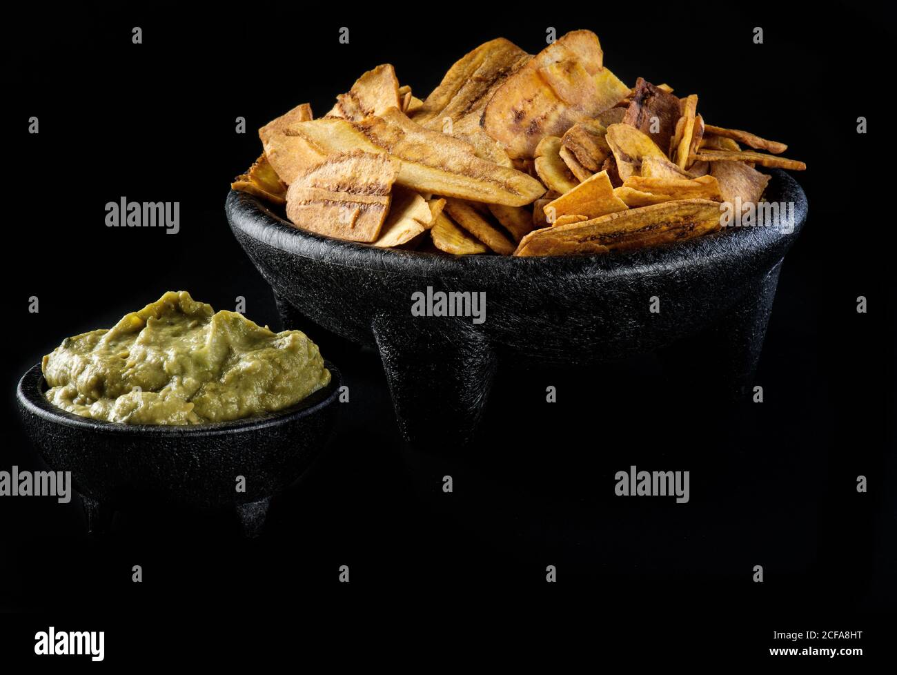 Bowl of fried plantains and guacamole on black table in modern restaurant Stock Photo
