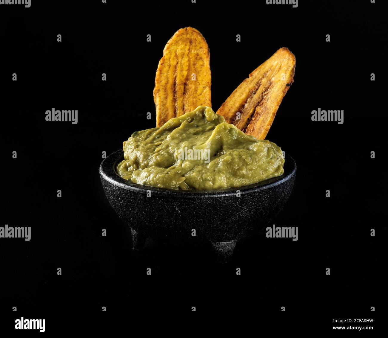 Bowl of fried plantains and guacamole on black table in modern restaurant Stock Photo