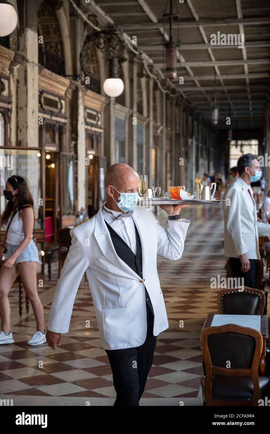 Venice. Italy. A waiter wearing a face mask during the Covid-19 pandemic delivers drinks at Caffè Florian on St Marks Square. Stock Photo