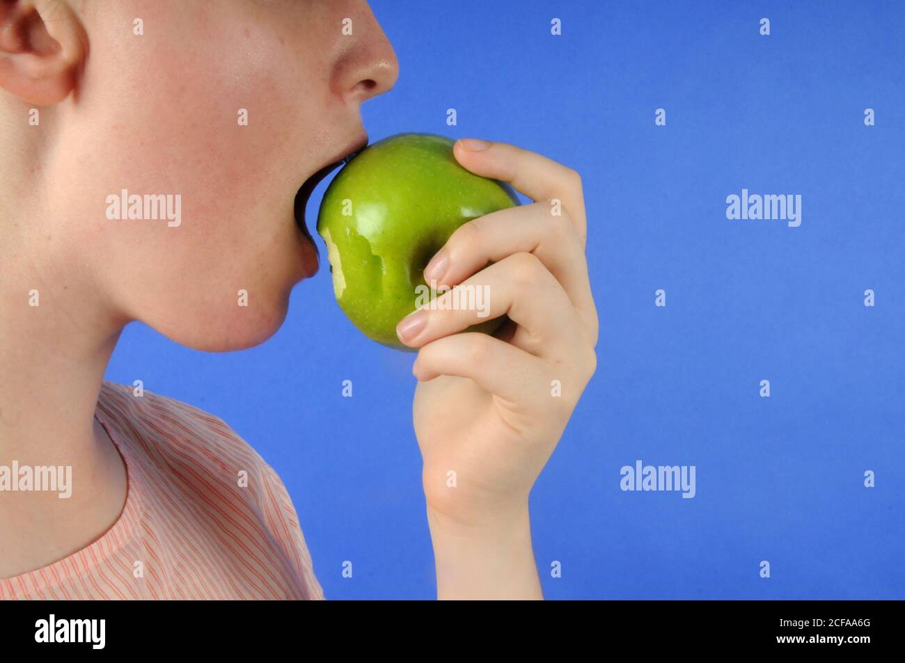 Side view of a girl taking a bite out of an green apple Stock Photo