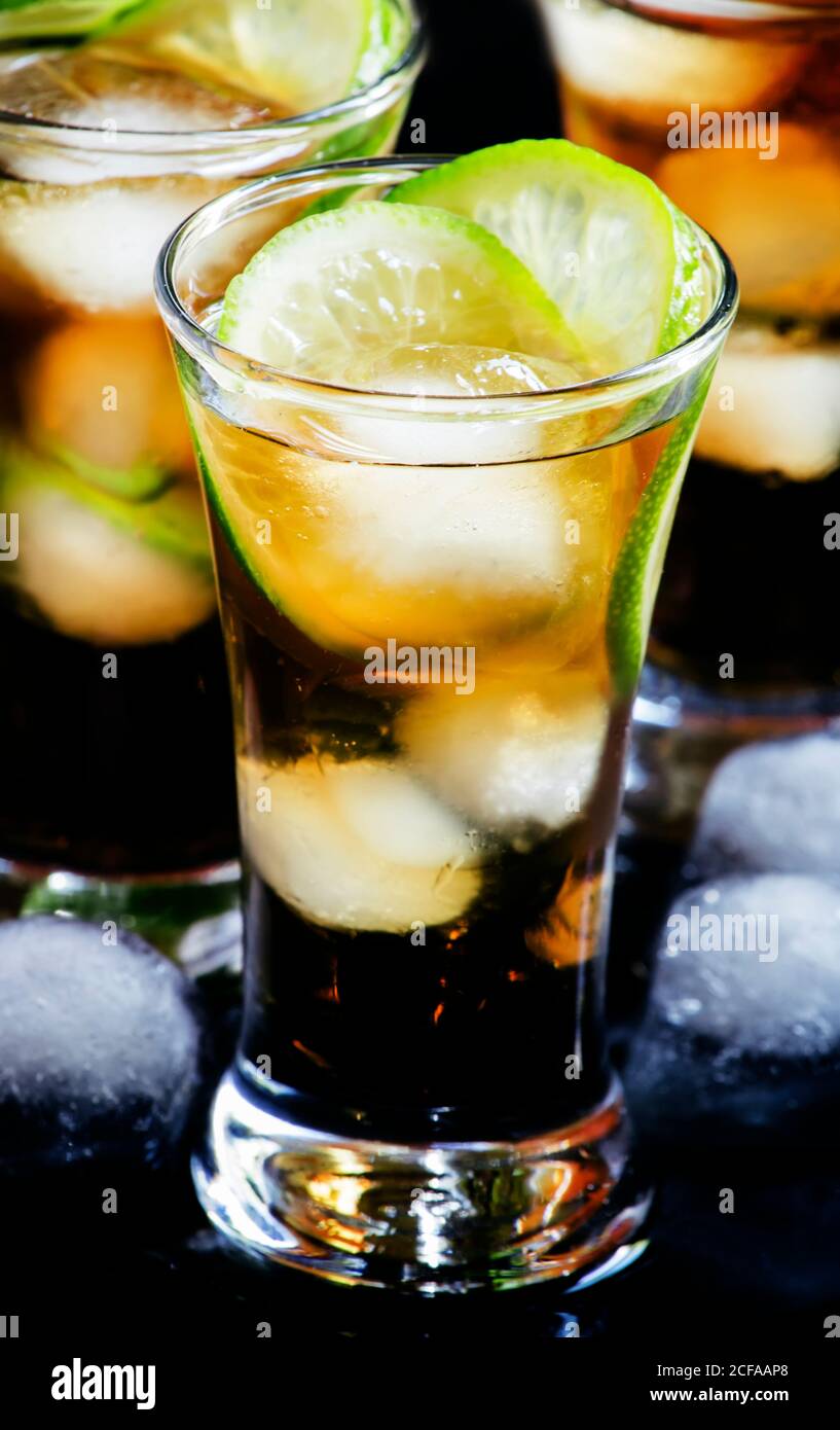 Alcoholic cocktail spiced rum with cola, lime and ice cubes, shaker, black background, selective focus Stock Photo