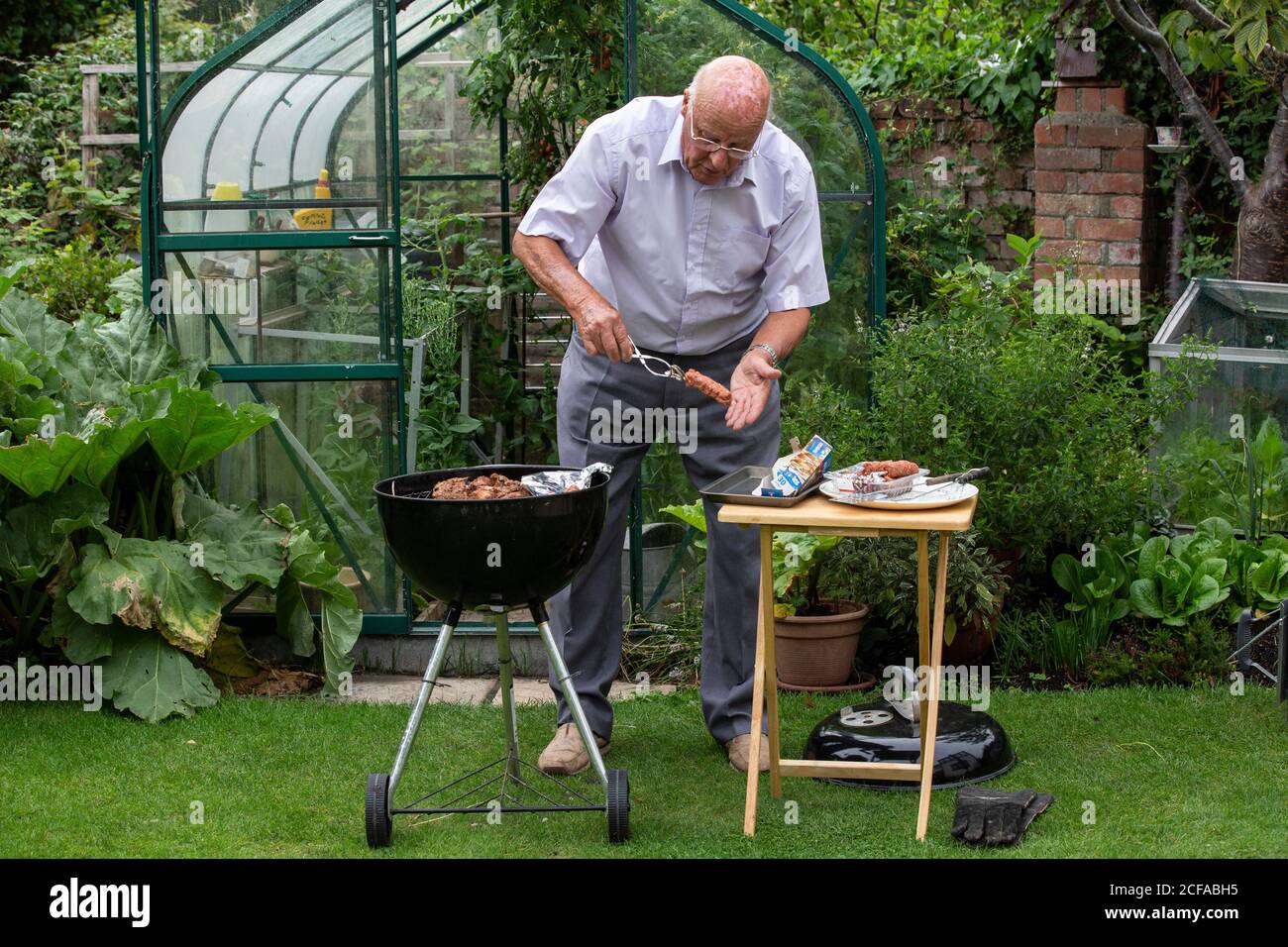 Retired pensioner in his 80's enjoying life outdoors barbecuing and eating healthy home grown vegetables during the coronavirus lockdown, Somerset UK Stock Photo