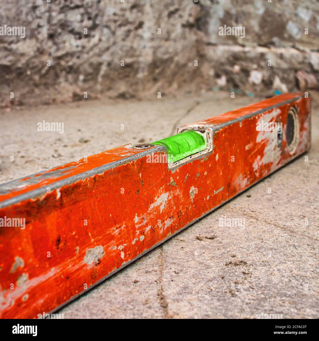 Used and dirty spirit level above a rough unfinished concrete wall Stock Photo