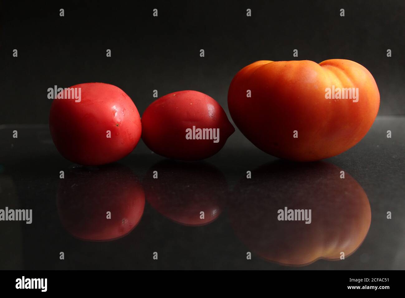 three red yellow tomatoes lie on a black background side view food background with copy space Stock Photo
