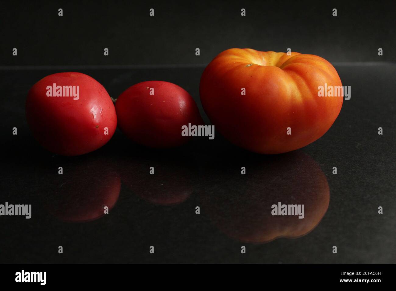 three red yellow tomatoes lie on a black background side view food background with copy space Stock Photo