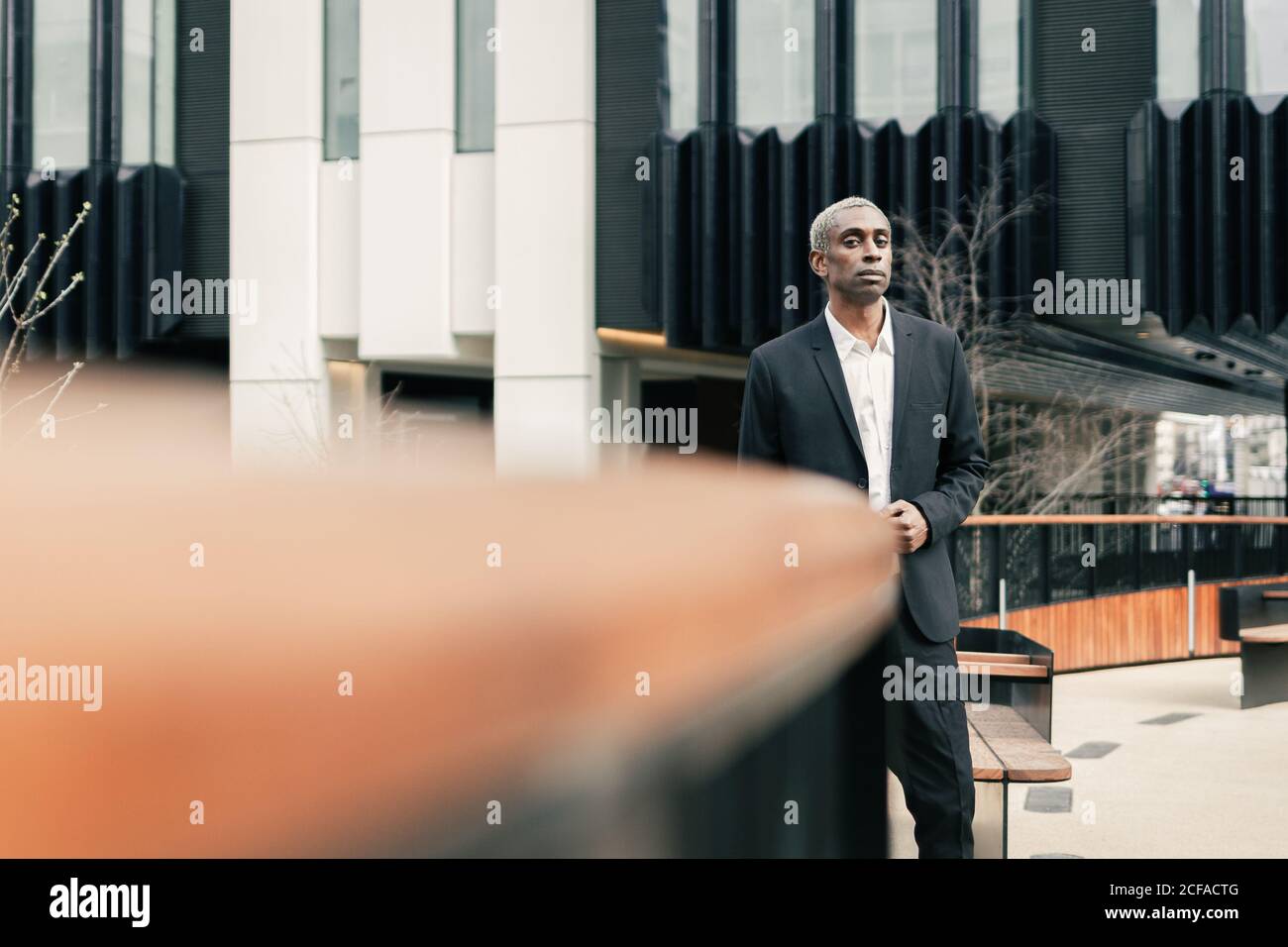 Confident black businessman leaning on railing Stock Photo - Alamy
