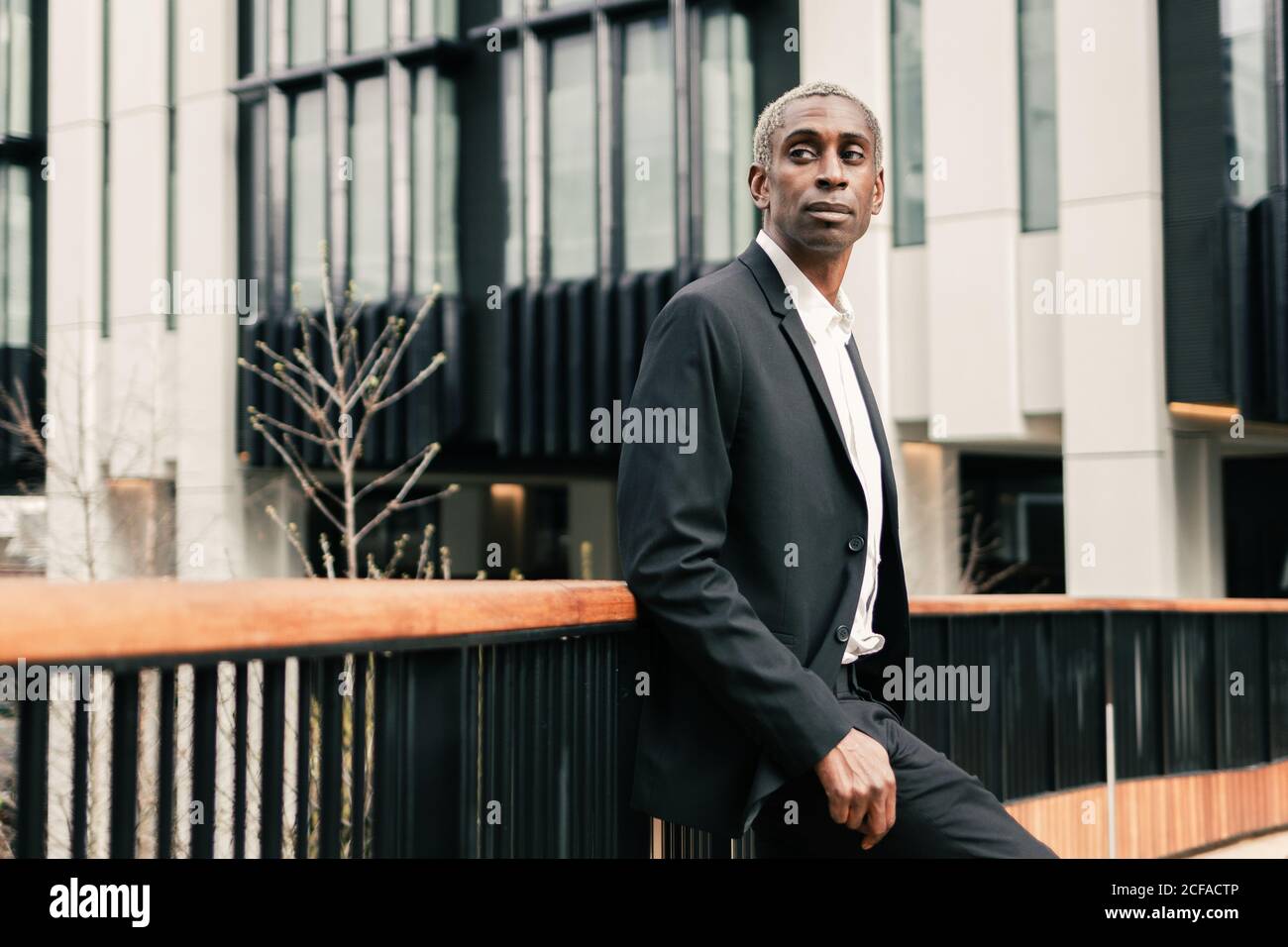 Confident black businessman leaning on railing Stock Photo - Alamy