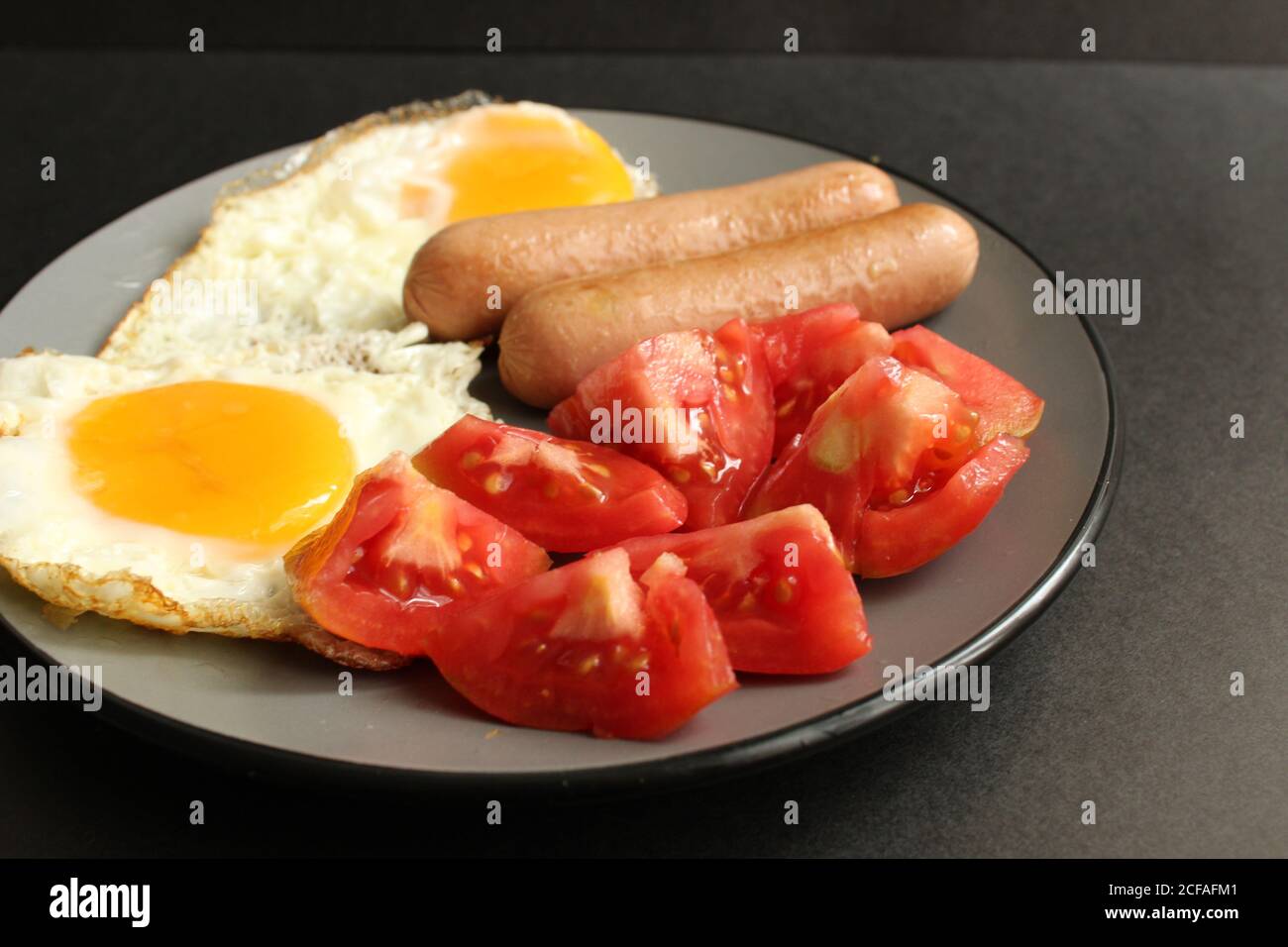 traditional English European Breakfast eggs sausage and salad vegetables red tomatoes on a gray plate on a black background close up side view Stock Photo