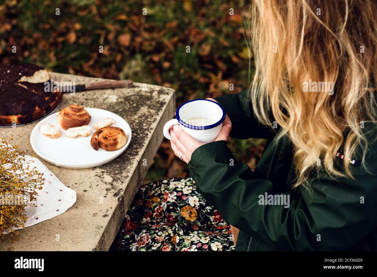 Side view from above of unrecognizable blond haired Woman in casual wear drinking milk during picnic with pastry in park Stock Photo