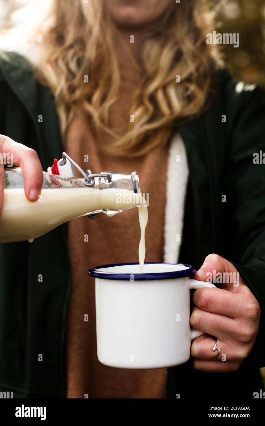 Blond haired faceless Woman in casual clothing pouring milk from bottle into mug during picnic Stock Photo