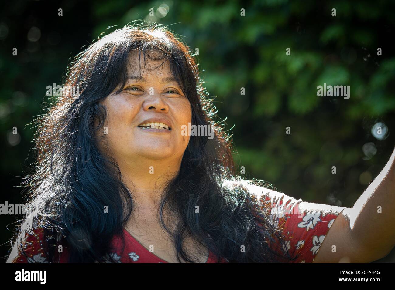Closeup picture of a middle-aged, in her 50s, Asian woman with soap bubbles. Green leaves in the background Stock Photo