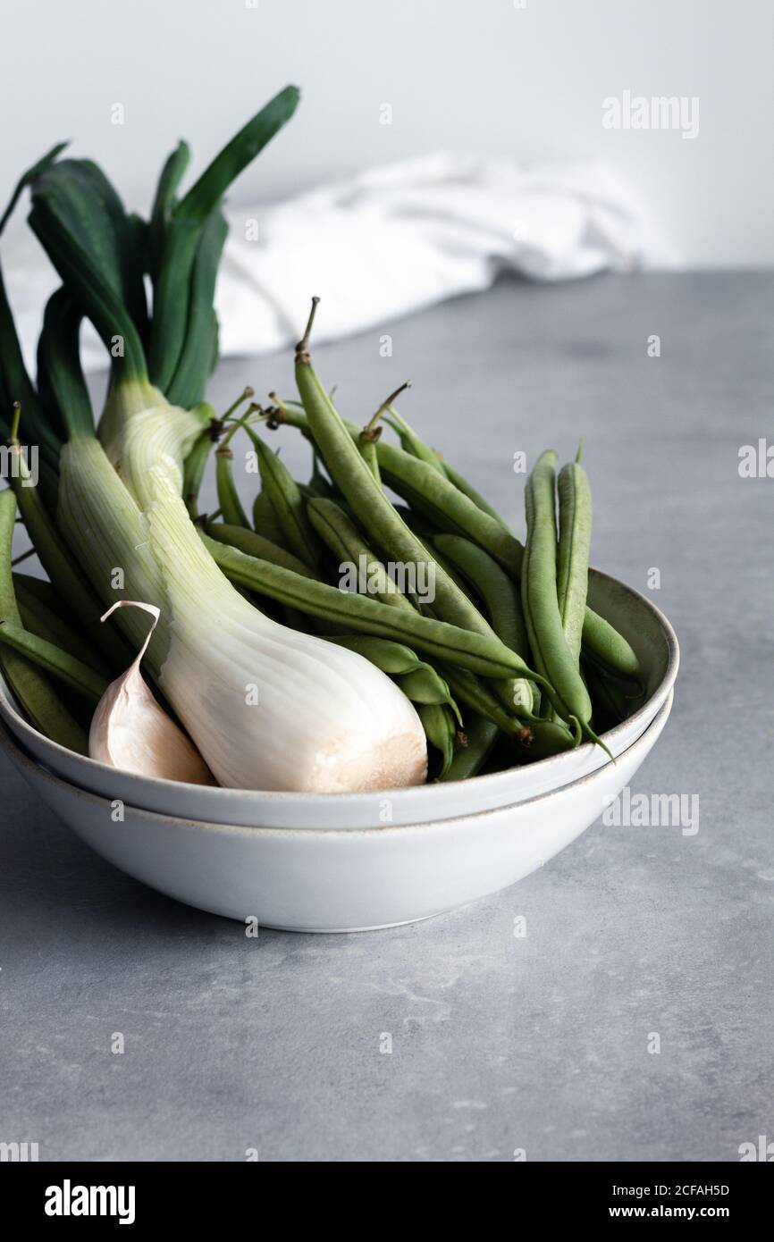 White bowl with garlic and green onion and green beans on table in kitchen Stock Photo
