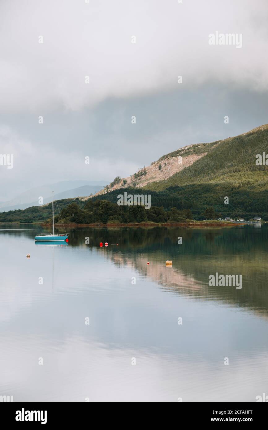 Picturesque landscape of mountain and cloudy sky reflected in tranquil water with sailboats in Glencoe on daytime Stock Photo