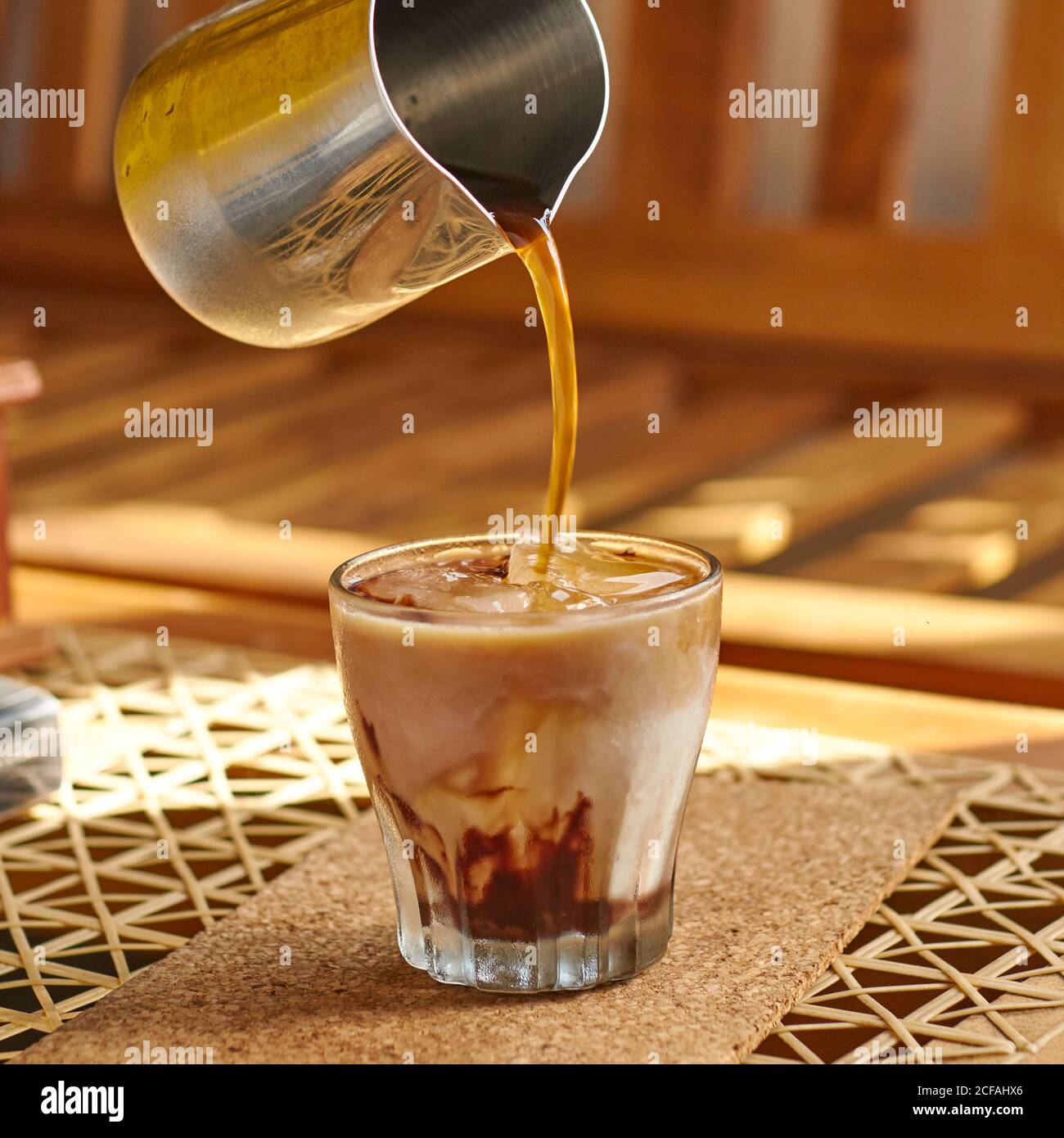 person pouring tasty hot drink from metal coffee pot into transparent glass with fresh milk and ice while preparing breakfast at home Stock Photo