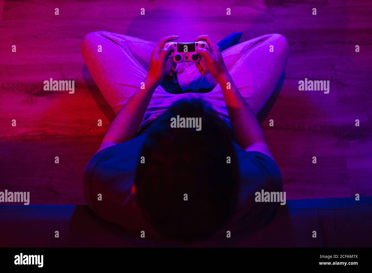 Top view of a boy sitting on the floor playing video games at night with colorful lights Stock