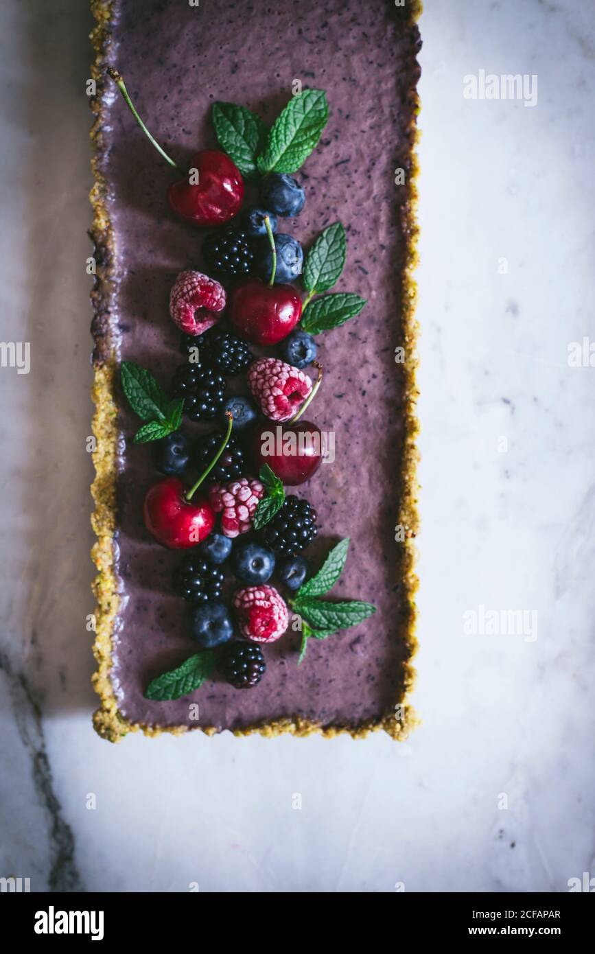 From above ripe tasty cherry blackberry blueberry raspberry with green stems on top of appetizing rectangular cake on white table Stock Photo