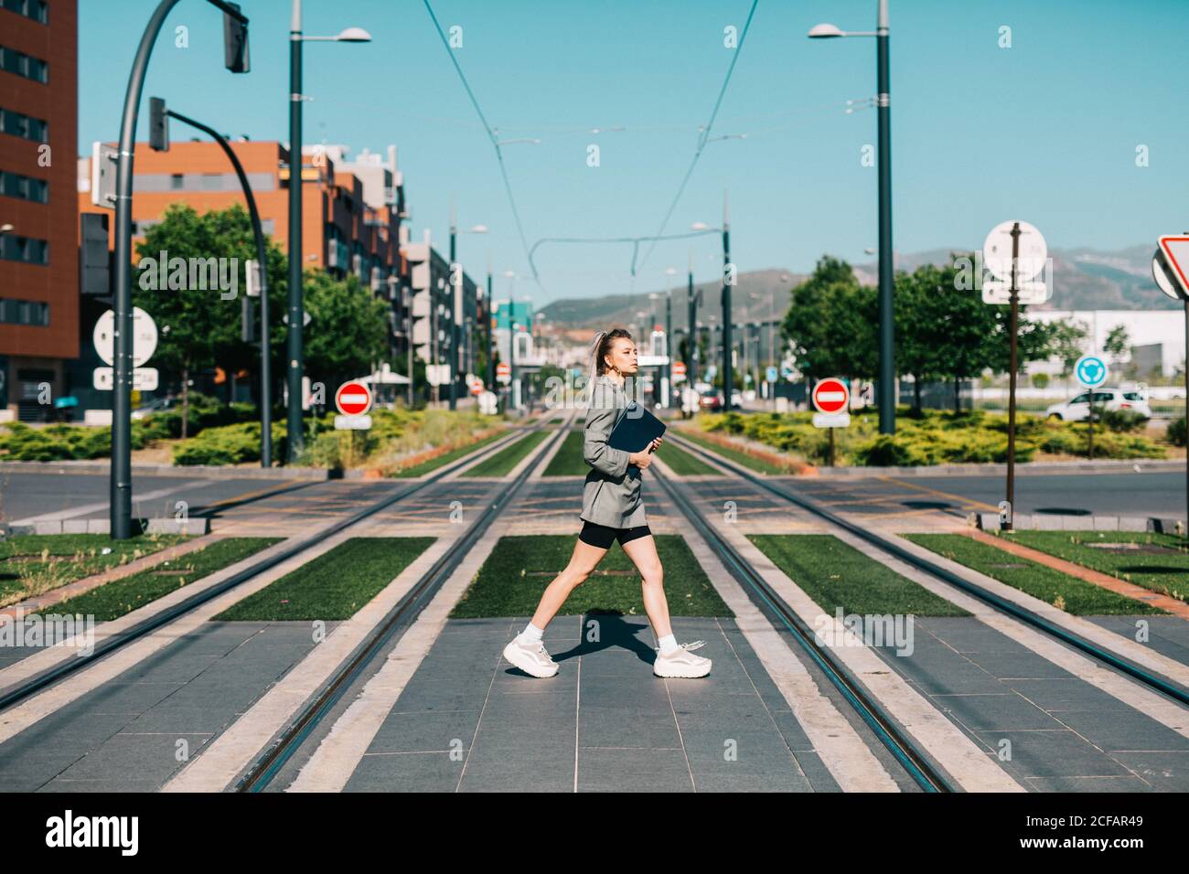 Side view of trendy Woman in stylish suit with black notebook fast crossing road looking around Stock Photo