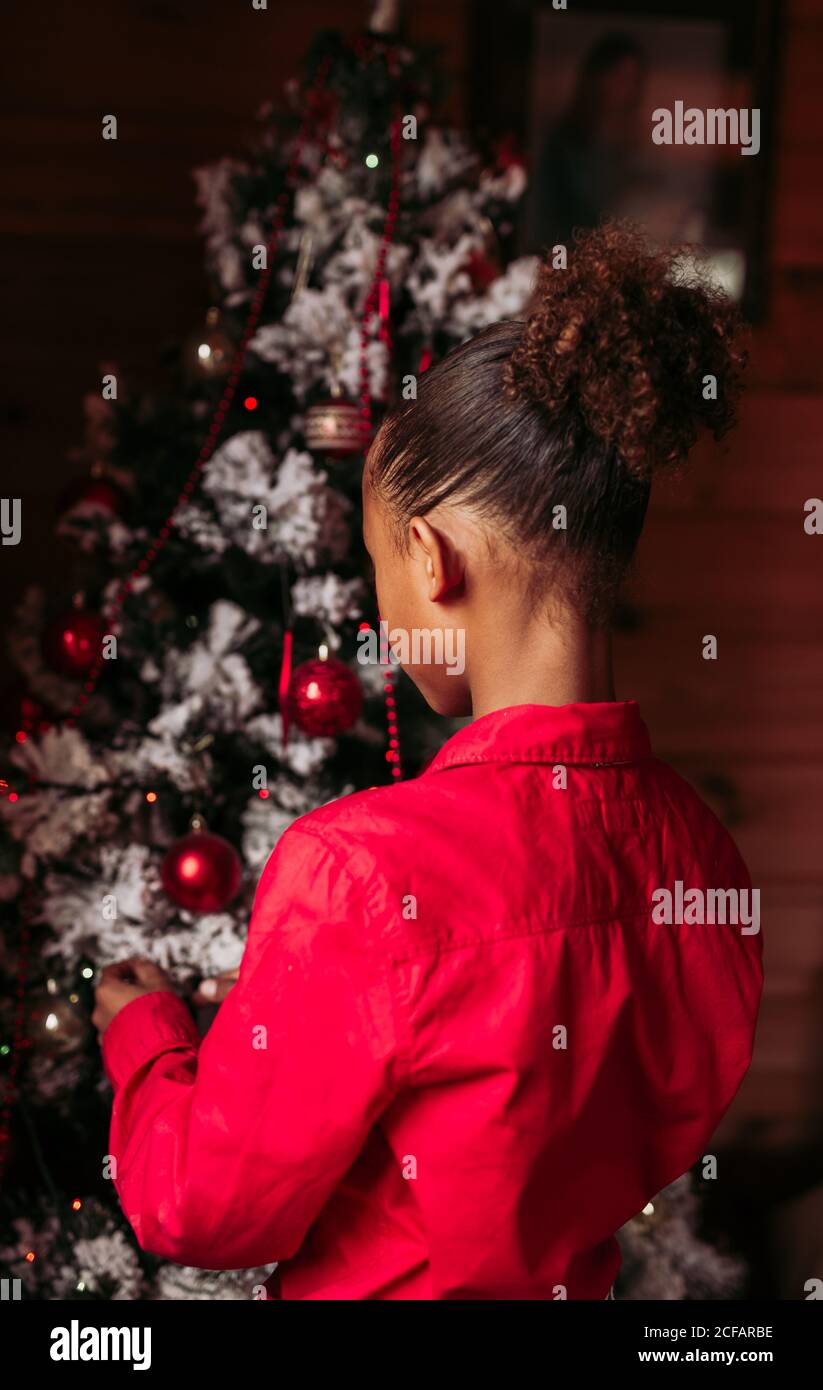 Back view of cheerful little black girl in red shirt looking at camera
