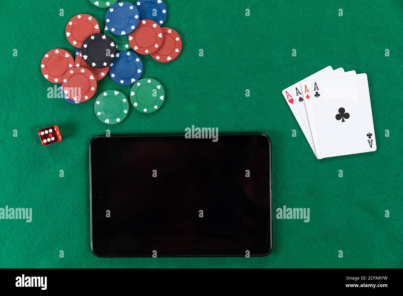 View of a black tablet, playing cards, a red dice and colorful tokens on plain green surface Stock Photo