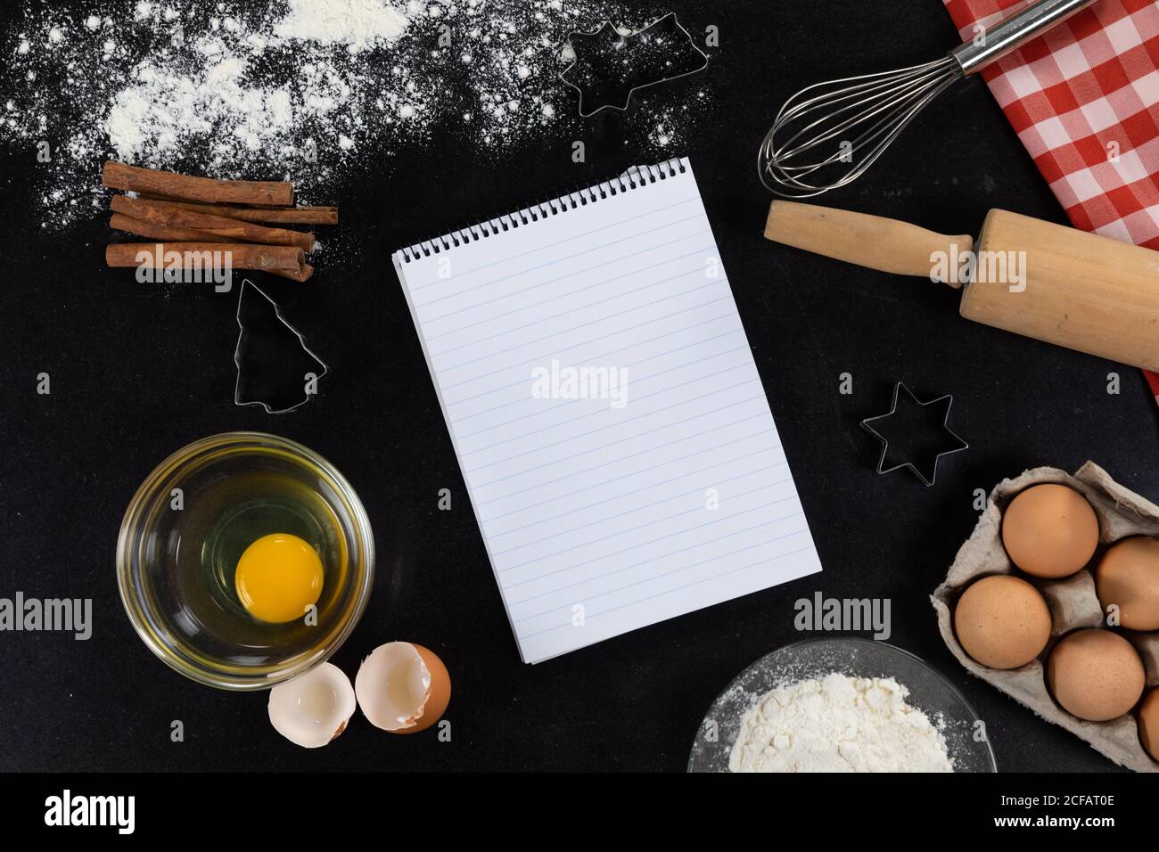 View of an empty notebook page with ingredients prepared for baking cookies, arranged on a plain bla Stock Photo