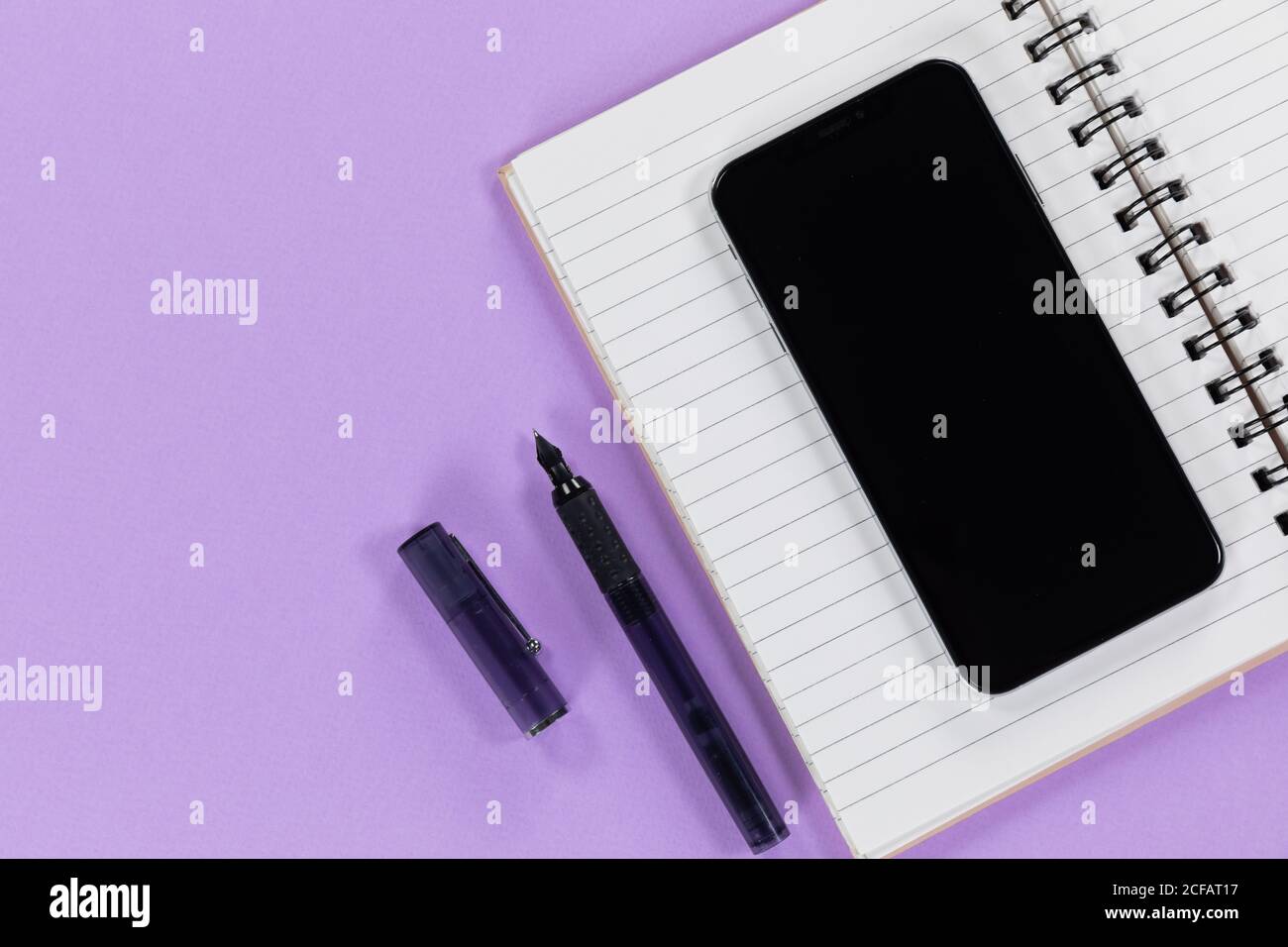 View of a black smartphone, a notebook and a black pen on plain purple background Stock Photo