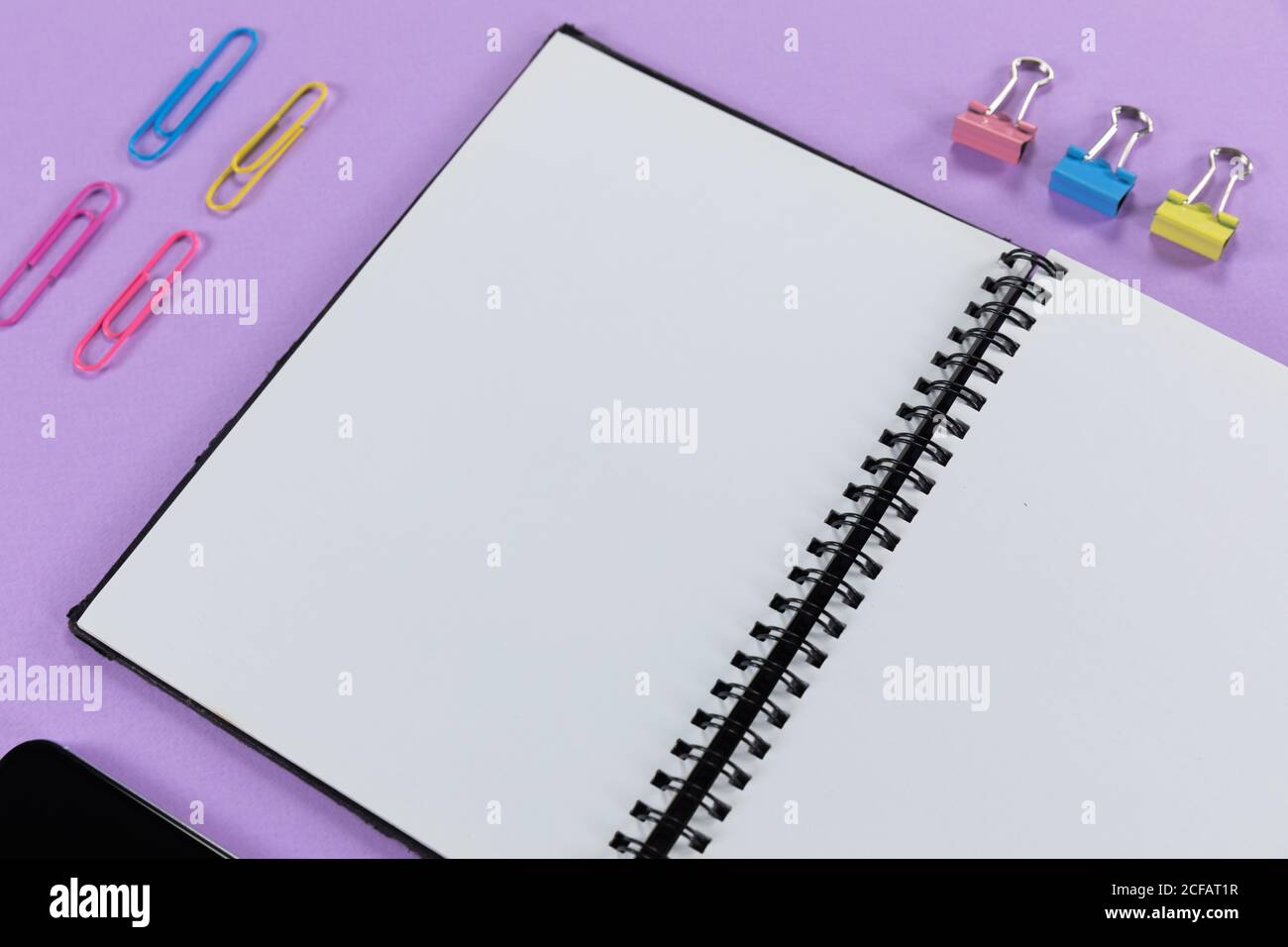 View of a notebook and colorful paperclips on plain purple background Stock Photo