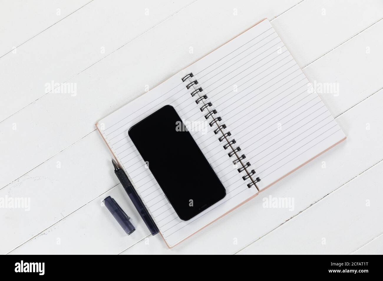 View of a black smartphone, a notebook and a black pen on plain white background Stock Photo