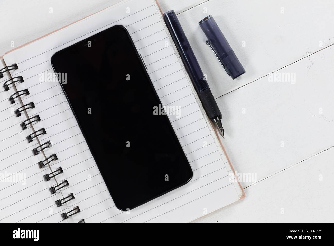 View of a black smartphone, a notebook and a black pen on plain white background Stock Photo