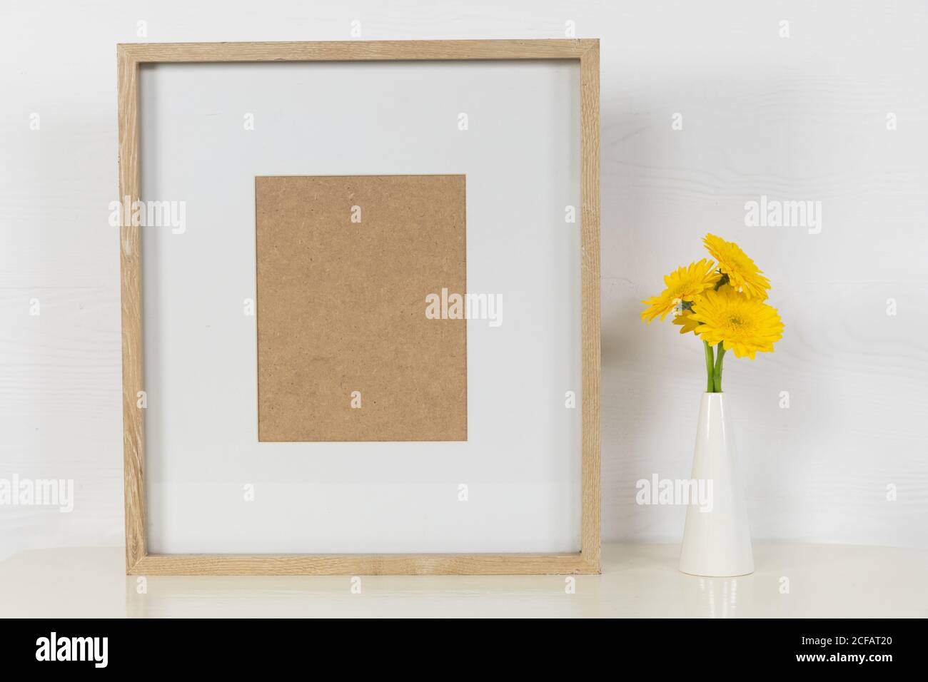 View of a picture frame, with yellow tulips placed in a glass vase on plain white background Stock Photo