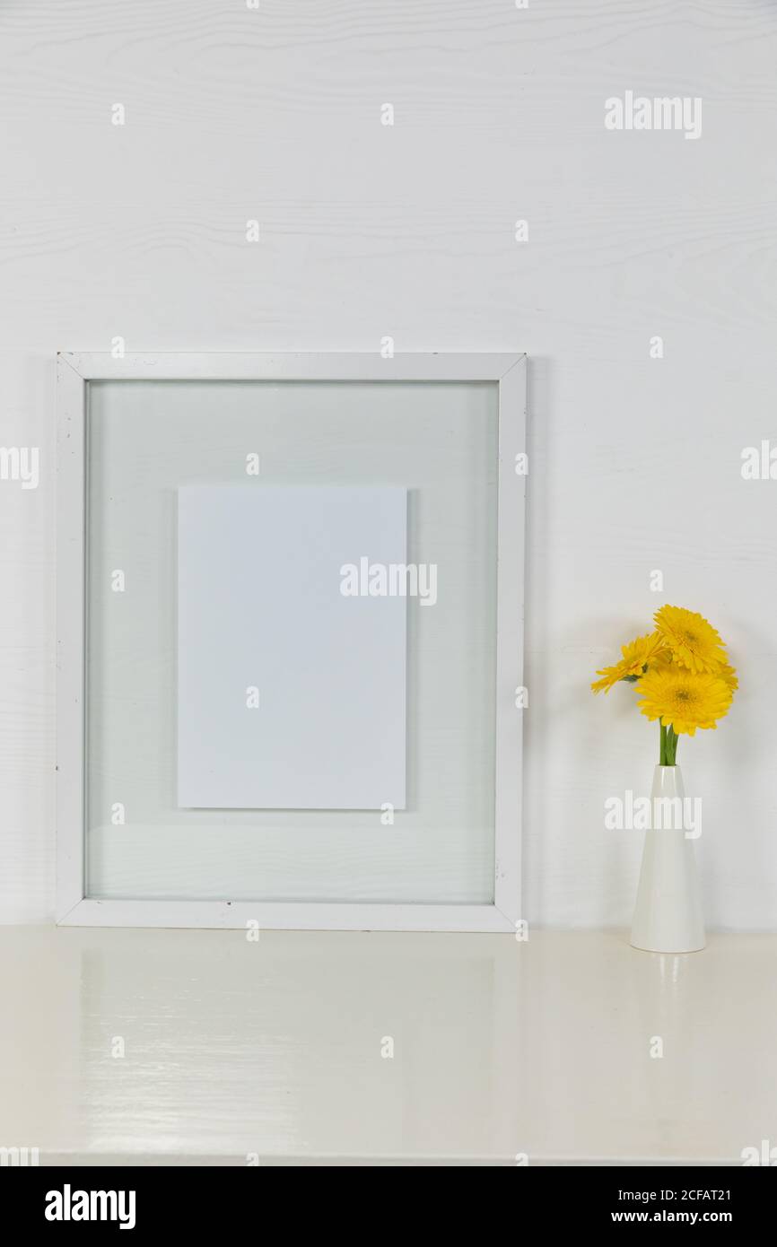 View of a picture frame, with yellow tulips placed in a glass vase on plain white background Stock Photo