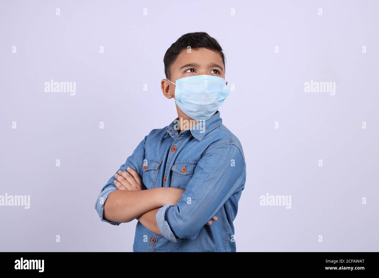 Cute little Indian boy with folded hands wearing surgical mask, looking up, isolated over white background Stock Photo
