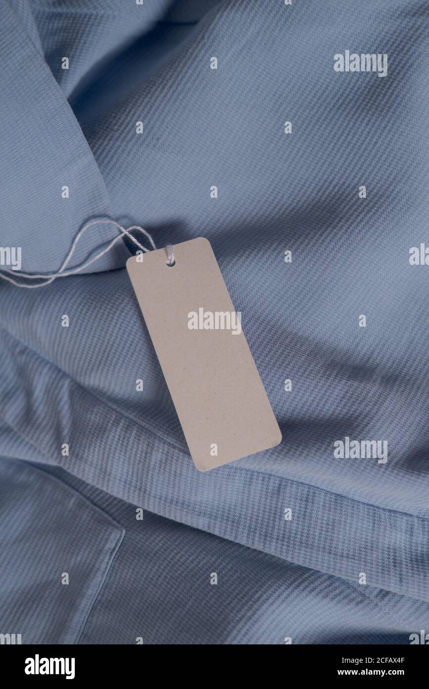 Clothing paper tag on ligh blue fabric. Fashion brand name mock up