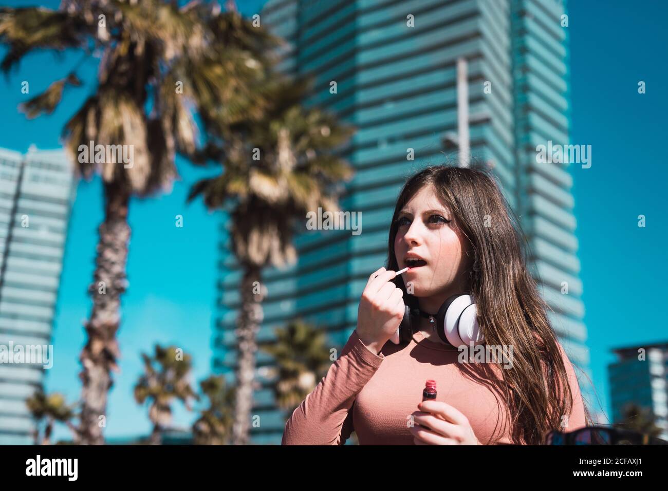 Attractive Woman putting lipstick in sunny city and looking away Stock Photo