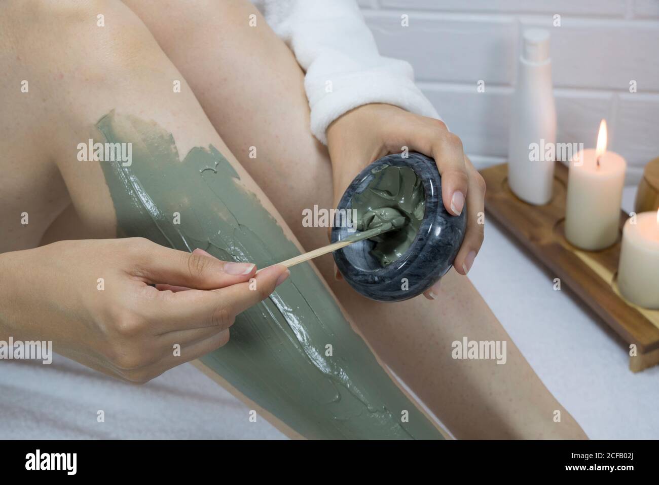 A woman applies a clay mask with a spatula to the skin of her legs. Irritation after depilation, shaving. Home skin care, body. SPA, moisturizing, tre Stock Photo