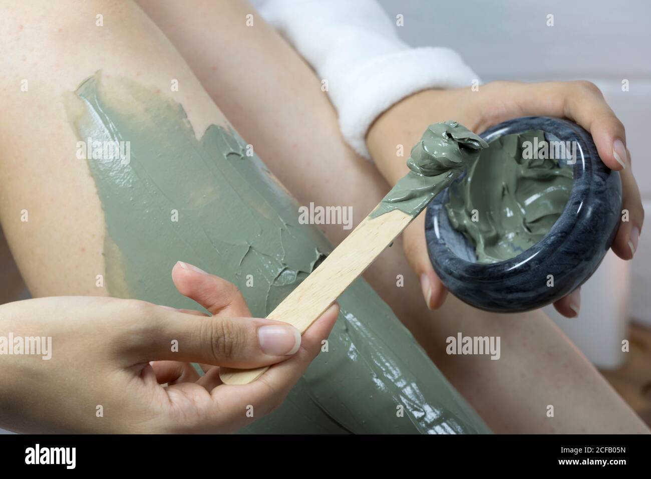 Home skin care, body.  A woman applies a clay mask with a spatula to the skin of her legs. Irritation after depilation, shaving. SPA, moisturizing, tr Stock Photo