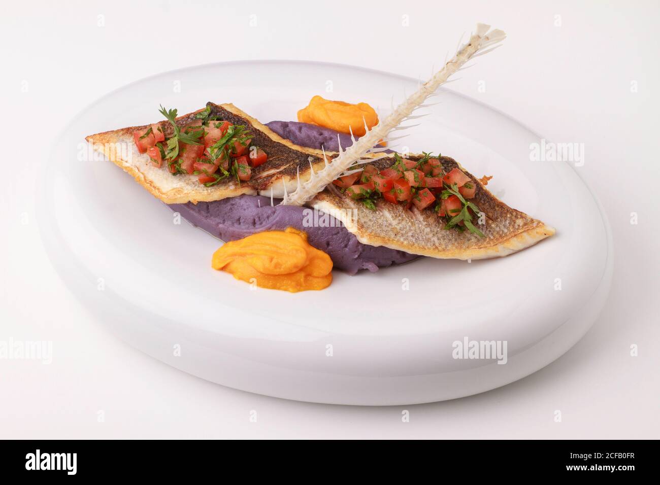 Sea bass fillet with purple potato puree, carrot puree and tomato salsa. Served on a white background. Stock Photo