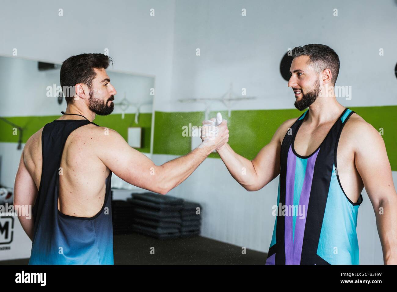Side view of muscular competitive male bodybuilders with powdered with talcum palms greeting  each other while standing in modern gym Stock Photo