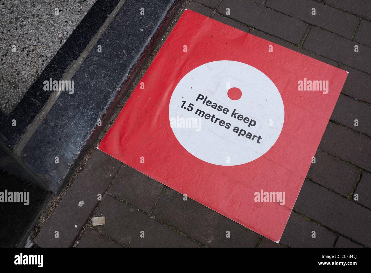 Red sticker on pavement 'Please keep 1.5 meter apart' in front of the threshold at the entrance of a shop. Coronavirus measures social distancing Stock Photo