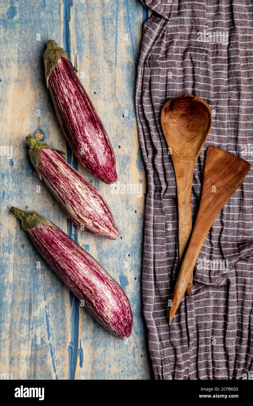 Set of fresh ripe eggplants placed near piece of striped cloth on weathered wooden tabletop Stock Photo
