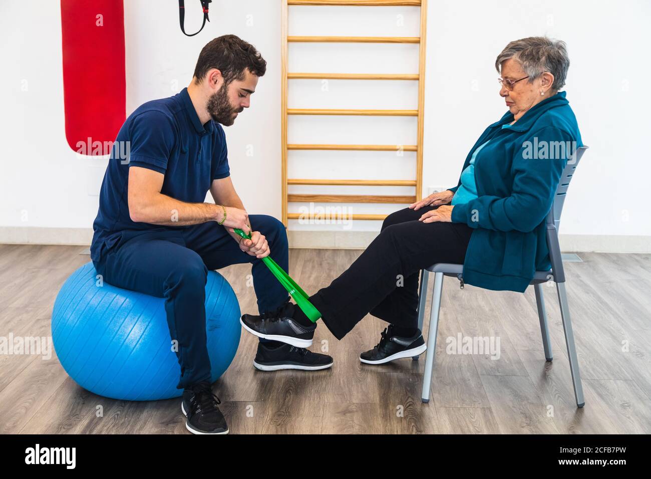 Side view of male personal coach sitting on exercise blue ball while