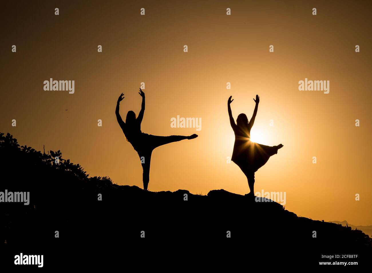 Young ballerinas with upped legs and hands dancing on hill in obscurity at sunset Stock Photo