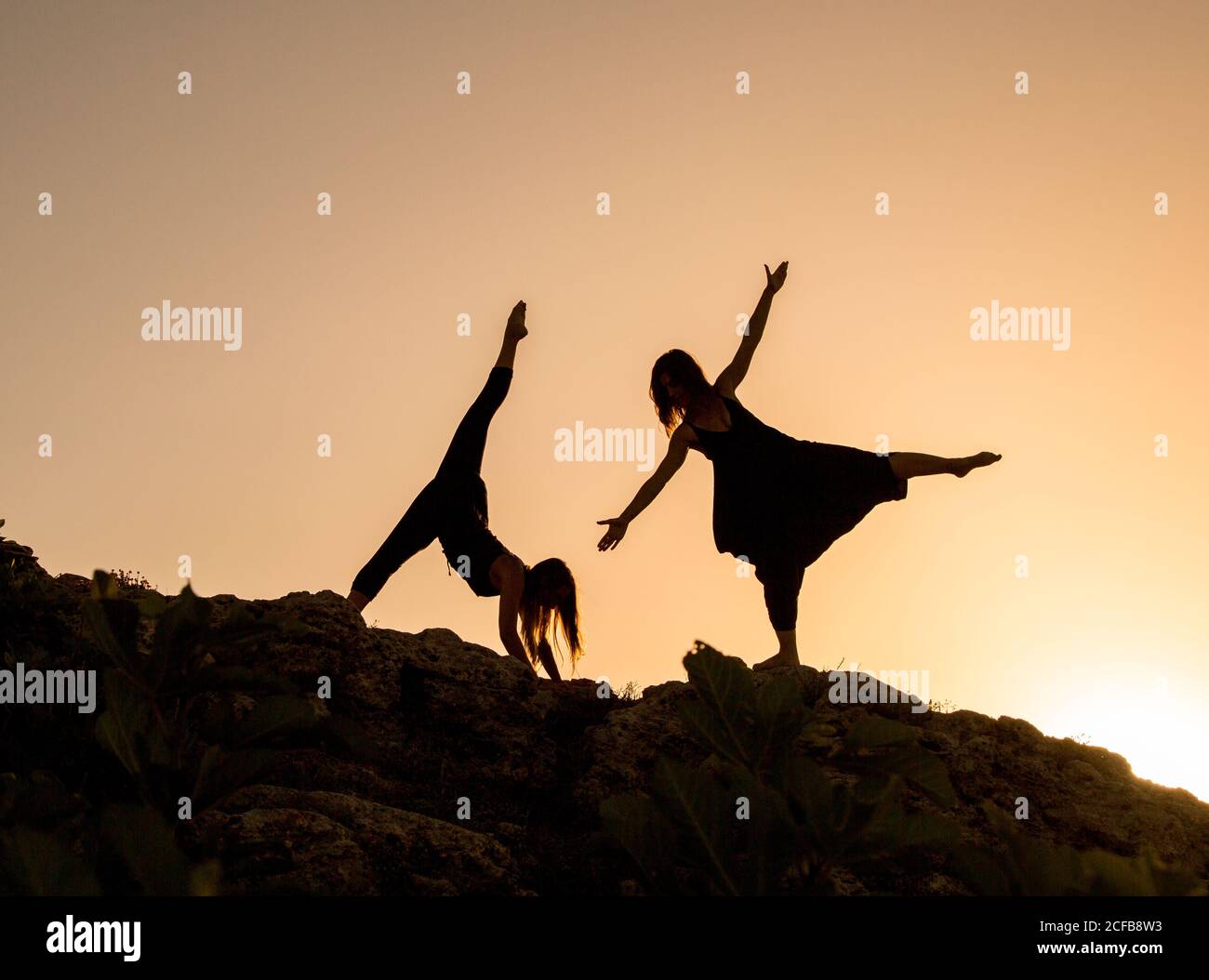 Young ballerinas with upped legs and hands dancing on hill in obscurity at sunset Stock Photo