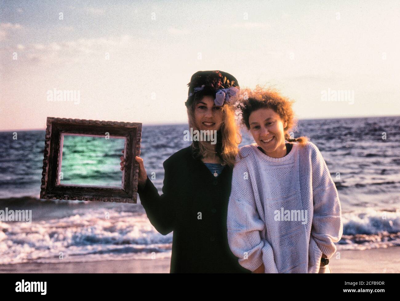 Two Young women stand near ocean with picture frame Stock Photo