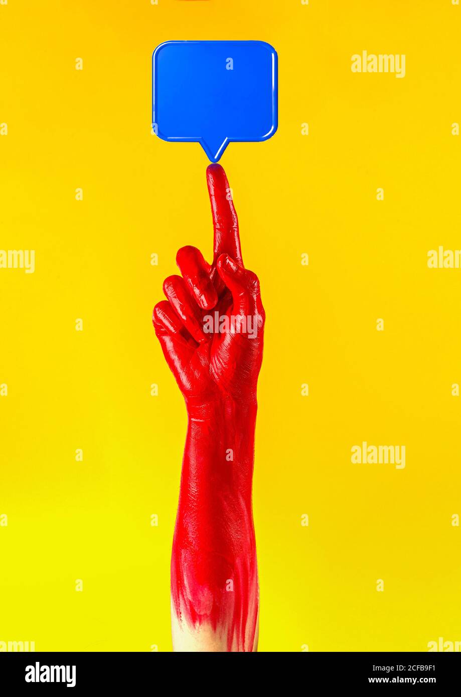 Crop person with red painted hand holding though balloon symbol on point up finger in studio on yellow background Stock Photo