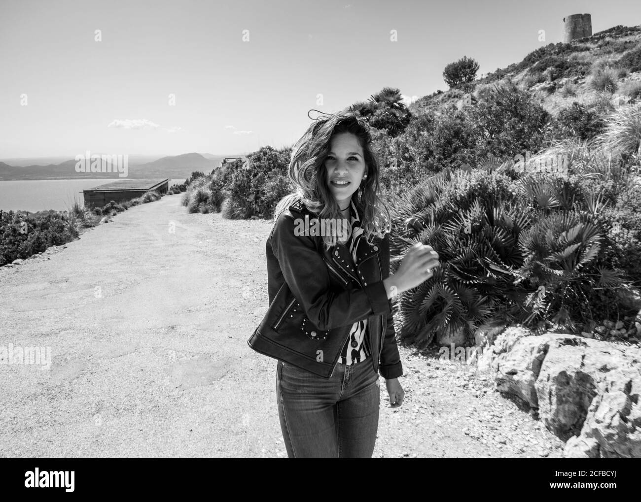 Black and white young Woman in casual outfit smiling and looking at camera while standing on coast of sea Stock Photo